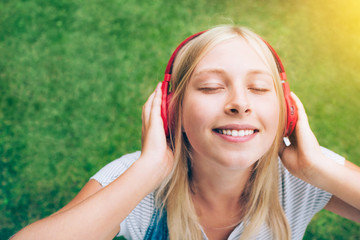 Pretty teenage girl in red headphones listening to music on green natural background.