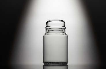 Empty glass jar on a black and white background with light effect