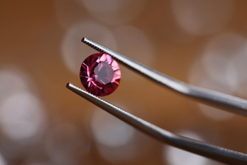 Jeweler in workshop holds pink stone in tweezers