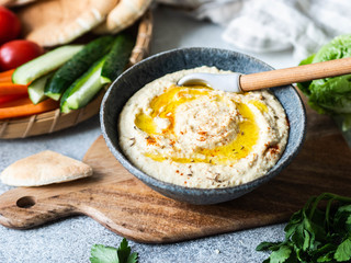 Homemade traditional spread hummus dip served with fresh vegetable , pita and herbs in tray on dark background.