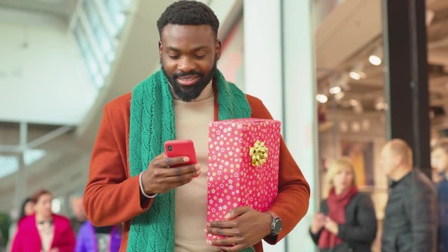 Slow motion african american young man use phone walk in mall Christmas time background Christmas tree feel happy smiling shopping internet face close up portrait mobile technology close up