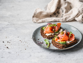 Healthy toasts with rye bread with cream cheese, salmon, fresh cucumber, capers, sesame seeds, black pepper and arugula on plate.