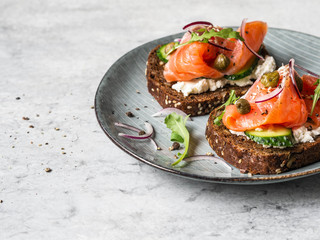 Healthy toasts with rye bread with cream cheese, salmon, fresh cucumber, capers, sesame seeds, black pepper and arugula on plate.