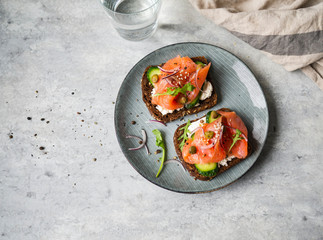Healthy toasts with rye bread with cream cheese, salmon, fresh cucumber, capers, sesame seeds, black pepper and arugula on plate.