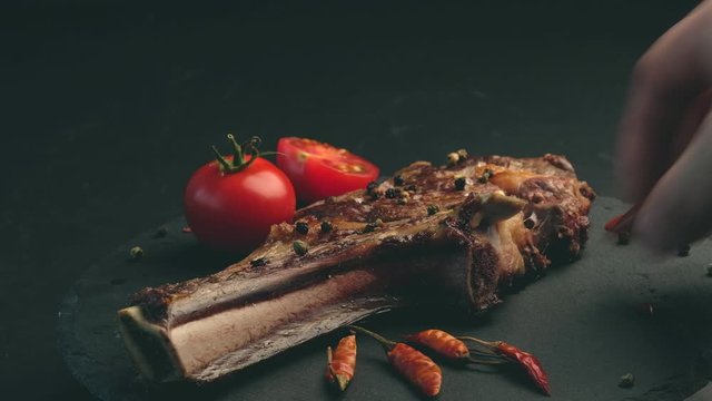 Delicious beef steak with rosemary, chili peeper and tomatoes on slate board. Roasted ribeye beef steak with herbs and vegetables