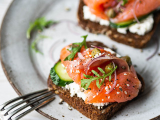 Healthy toasts with rye bread with cream cheese, salmon, fresh cucumber, capers, sesame seeds, black pepper and arugula