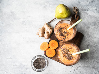 Two glasses of fresh healthy carrot, pear, ginger smoothie with chia seeds on a grey background. Top view