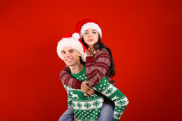 Studio portrait of young couple, boyfriend & girlfriend wearing santa claus hat & ugly christmas sweater. Holiday outfit w/ snowflake pattern print. Close up, copy space for text, isolated background.