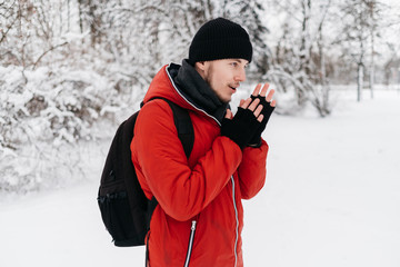 Young Man in Black Hat and Red Down Jacket Warming His Hands in The Winter Park