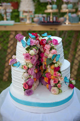 Wedding cake decorated with colorfull roses. Celebration party concept. flowers in the middle of the place where the cake is cut on the blue butterfly . White cake with rounded . Two-layer cake .