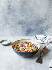 Red cabbage, carrot, cabbage coleslaw salad in blue bowl on grey background.
