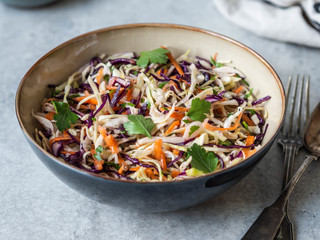 Red cabbage, carrot, cabbage coleslaw salad in blue bowl on grey background.