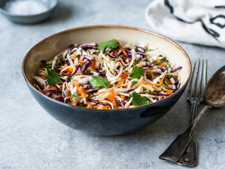 Red cabbage, carrot, cabbage coleslaw salad in blue bowl on grey background.