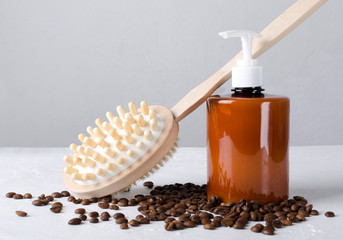 Closeup of brown bottle of cosmetic product, coffee beans and brush for massage on the white surface.Concept of beauty treatments with natural ingredients