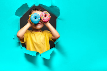 Happy cute boy is having fun played with donuts on black background wall. - obrazy, fototapety, plakaty