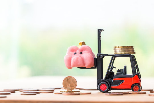 happy piggy bank on stack coins with miniature toy forklift machine, over blurred green spring garden background.image for saving money concept.
