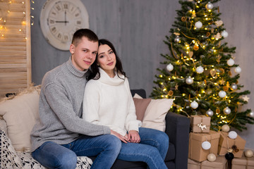 Obraz premium christmas and love concept - portrait of beautiful couple sitting in living room with Christmas tree