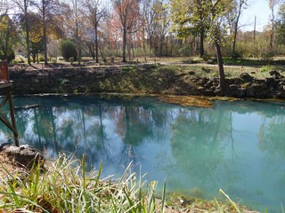 Wide scenic shot of the clear blue waters of a spring, with the colorful trees reflected in the...