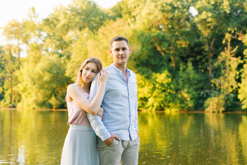 Romantic couple in love guy and girl in the summer in the Park on the background of the lake. Newly married couple. The girl hugs the guy from behind and clings to him and