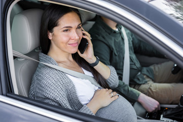 Fototapeta na wymiar Beautiful pregnant woman is talking in the phone in the car