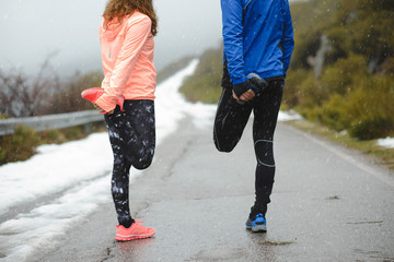 Close up of couple of runners stretching legs for warming up before running in winter mountain road...