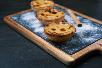 pasteis de nata, pasteis de belém, typical Portuguese dessert and a cinnamon stick over a blackboard table