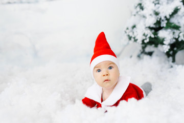 The surprised look of a small child in a Santa suit lying in artificial snow. Christmas or new year card with copy space