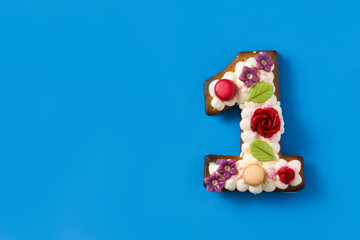 Number one cake decorated with flowers and cookies on blue background. Copy space