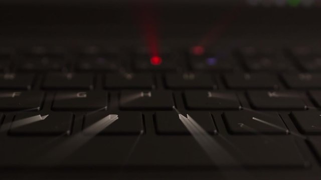 illuminated keyboard buttons letters in multiple RGB colors on modern black laptop with iridescent beams of light coming from the red green blue yellow and orange light 