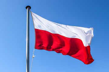 Polish flag on a flagpole waving in the wind, close up, on a clear blue sky day isolated