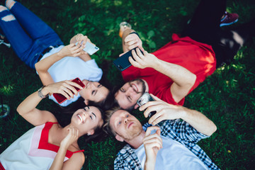 Joyful hipsters having relax on grass while browsing smartphones at park