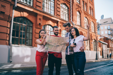 Happy adult tourists asking for advice locals while using map on street in sunny summer day