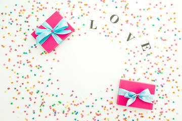 Valentines day composition with love word, gift box and colorful confetti on white background. Copy space. Flat lay