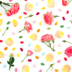 Roses flowers and orange petals with bright candy on white. Flat lay, top view.