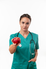 Beautiful female doctor in green uniform. Portrait of nurse holding an apple. 