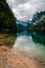Beatiful view over the Gosau see in Austria towards Dachstein mountain, during fall with cloudy weather over the mountains, sand beach in the foreground