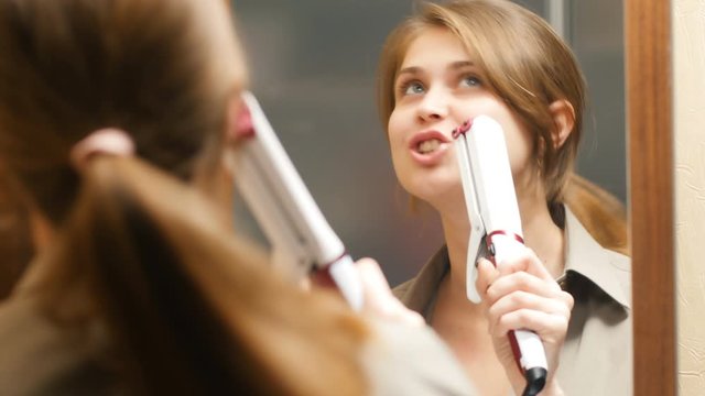 reflection of a beautiful cute girl fooling around and singing in a hair styler as if in a microphone in front of a mirror, the concept of beauty and female mood