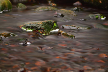 Green mossy rocks in dark moorland water. Long exposure photography, capturing motion. Soft, smooth forest river landscape background. 