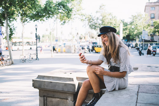 Positive hipster girl - lover of travelling and exploring new cities taking rest on Barcelona streets for clicking selfie pictures via cellphone front camera for capture good moment in memory