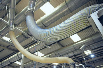 Plastic ribbed air conditioning airflow pipes and tubing sucking dust and industrial particles out of wood and metal cutting machines. Keeping the air and workplace clean and free from pollution