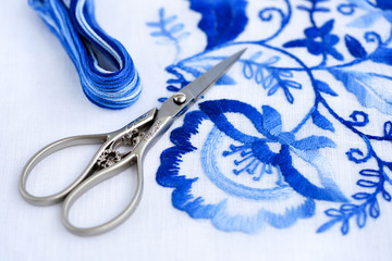 Embroidery, thread and scissors. Blue floral ornament on a white background. Art and craft...
