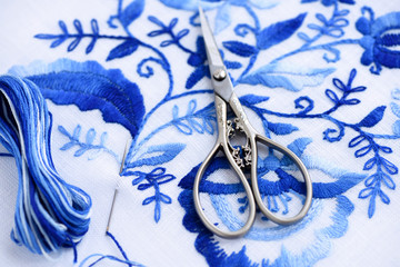 Embroidery, scissors, sewing needle and thread. Blue floral ornament on a white background. Art and craft conception.