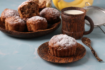 Banana muffins with oatmeal flakes sprinkled with icing sugar on a coconut plate and cup of milk, horizontal orientation
