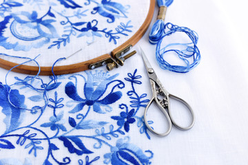 Embroidery hoop with fabric, sewing needle and thread. Handmade Embroidery pattern of blue flowers on a white background