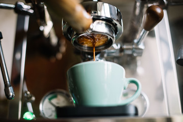 Delicious fresh morning espresso coffee with beautiful crema puring through the bottomless portafilter with wooden handle into ceramic green cup