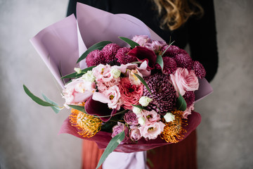 Very nice young woman holding big beautiful bouquet of fresh roses, carnations, eustoma, cymbidium, protea, chrysanthemum, eucalyptus, david austin roses flowers in colors pink and burgundy colors