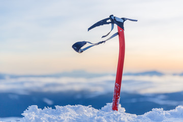 Expedition equipment for winter climbing - ice-axe in natural conditions at stunning sunset scene in mountains background. - obrazy, fototapety, plakaty