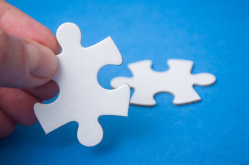 Obraz premium Closeup of man connecting with hand two jigsaw puzzle pieces on blue background. The concept of finding the right solutions in teamwork.