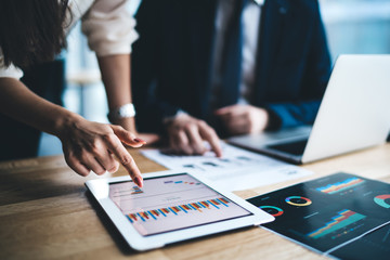 Young businessman and woman in formal sitting in office using tablet working on financial charts in...
