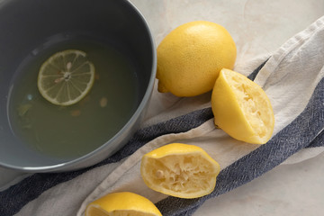 Lemons and fresh juice in gray bowl on marble table background and kitchen towel, above. Make lemonade concept. Healthy drink and food. Natural vitamin C